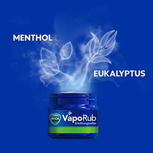 Ein offener Tiegel von WICK VapoRub Erkältungssalbe, Dämpfe steigen auf, daneben steht Eukalyptus und Menthol