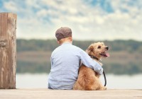 Junge sitzt bei Reise mit Hund auf einem Seesteg