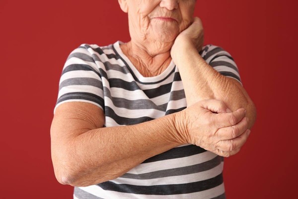 Frau mit Osteoporose hält sich den Ellbogen