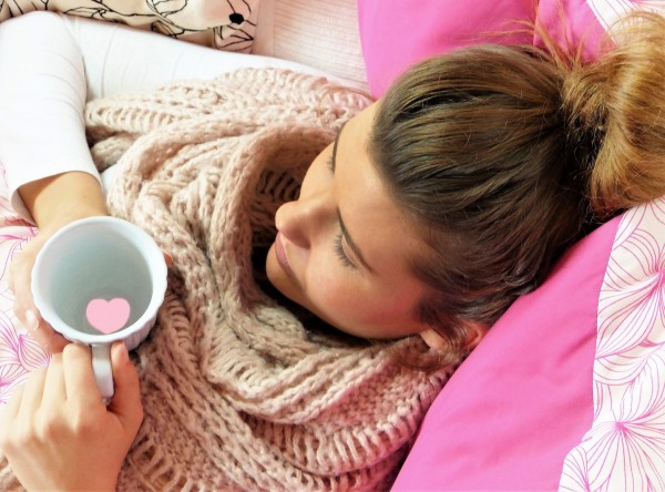Frau liegt mit einer Tasse Tee im Bett, um ihre Erkältung schnell loszuwerden