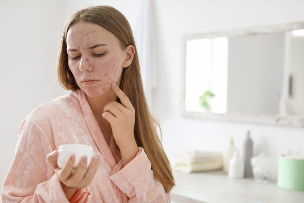 Frau mit Allergie im Gesicht begutachtet ihre Kosmetik im Badezimmer.