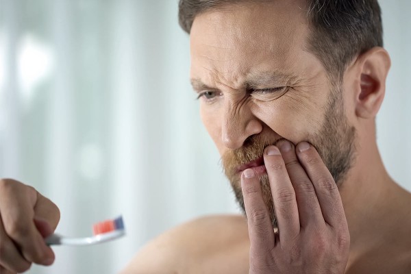 Mann mit Zahnfleischentzündung hält sich beim Zähneputzen den Mund.
