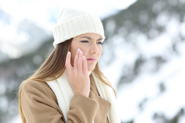 Frau fasst sich beim Winterspaziergang an ihre trockene Haut im Gesicht.