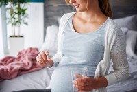 Eine schwangere Frau hält ein Glas Wasser und ein Nahrungsergänzungsmittel in ihren Händen. 