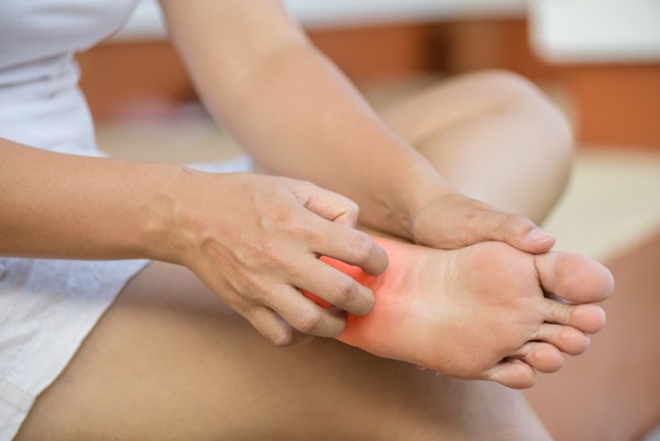 Frau mit Neurodermitis am Fuß kratzt ihre Fußsohle.