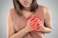 Frau mit Herzinfarkt hat Luftnot, hält sich den Brustkorb und den Oberbauch