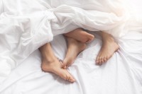 Füße eines Pärchens schauen unter der Bettdecke hervor