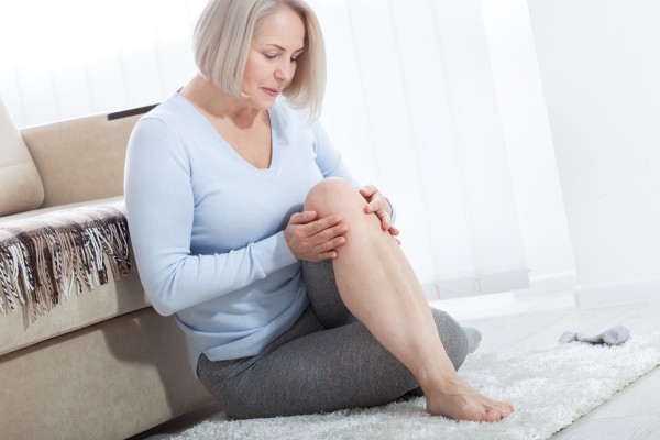 Frau hält sich ihr Knie wegen Gelenkschmerzen in den Wechseljahren