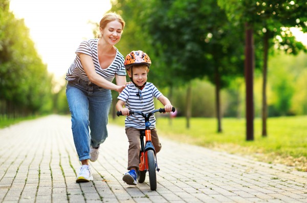 Frau, die Wert auf Bewegung und Gesundheit legt, unterstützt ihr Kind beim Fahrradfahren.