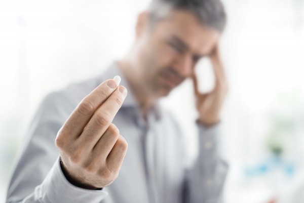 Mann hält Schmerzmittel gegen Kopfschmerzen in der Hand.