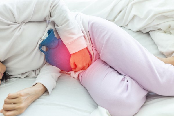 Frau mit ansteckender Blasenentzündung liegt mit Wärmflasche im Bett.