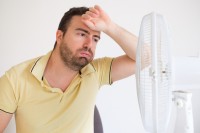 Mann steht vor dem Ventilator und wünscht sich Tipps gegen Schwitzen