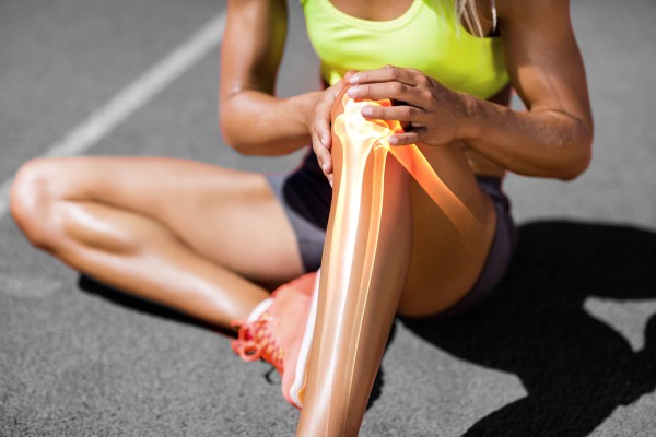 Frau mit Sportverletzung hält sich ihr schmerzendes Knie.